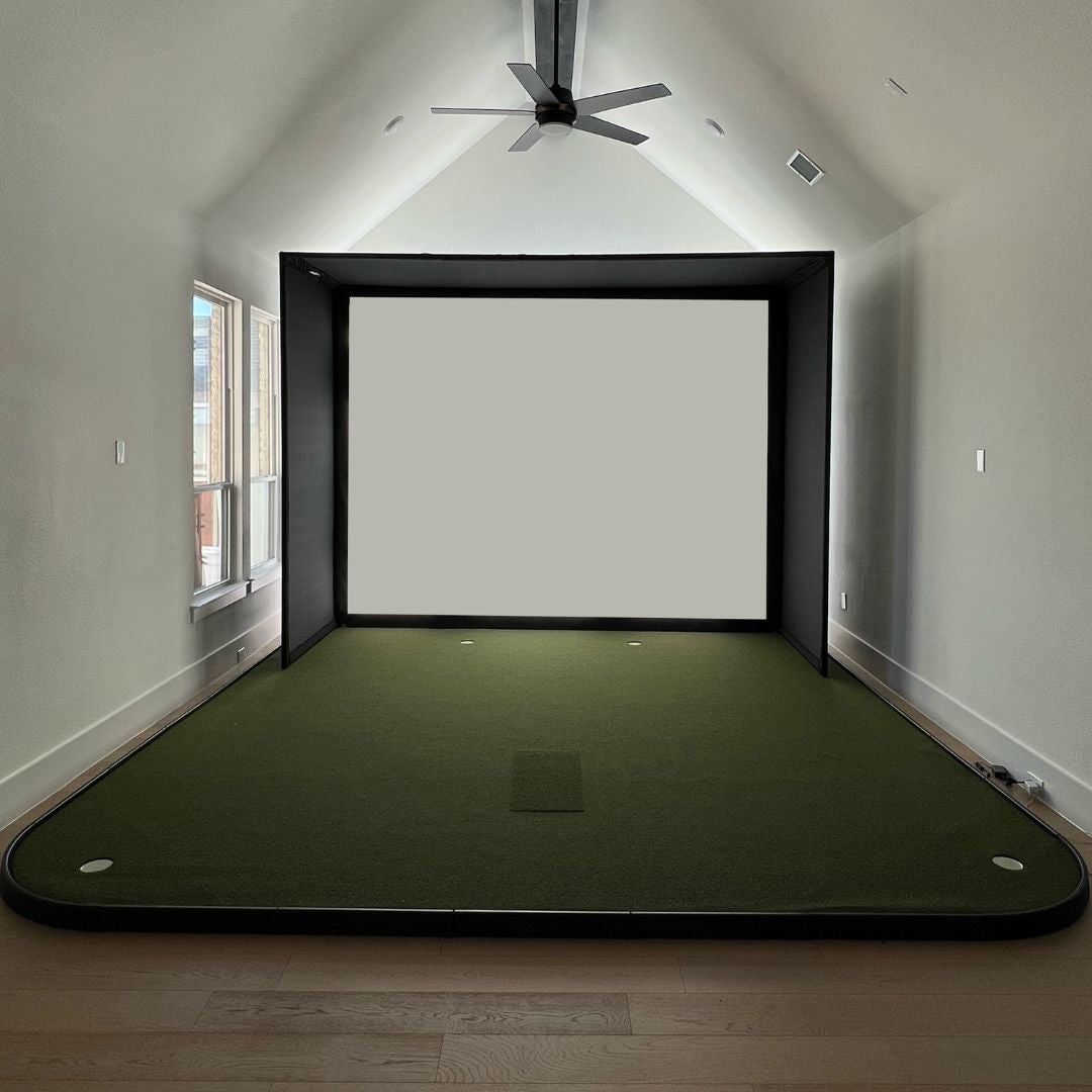 Front view of a golf simulator enclosure with an impact screen and golf mat in a living room.