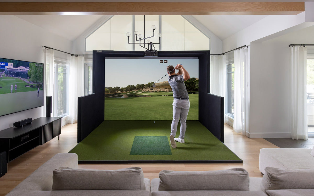 Front view of a home golfer swinging inside a living room, using the Simbooth 2 kit setup.